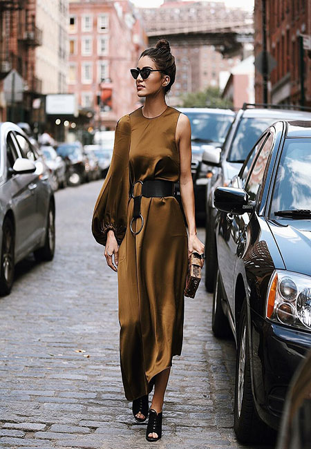 Модный лук: Ассиметричное атласное коричневое платье с широким поясом и черные босоножки на шнуровке, коричневый клатч-книжка, кольцо с квадратным камнем, солнцезащитные очки кошачий глаз