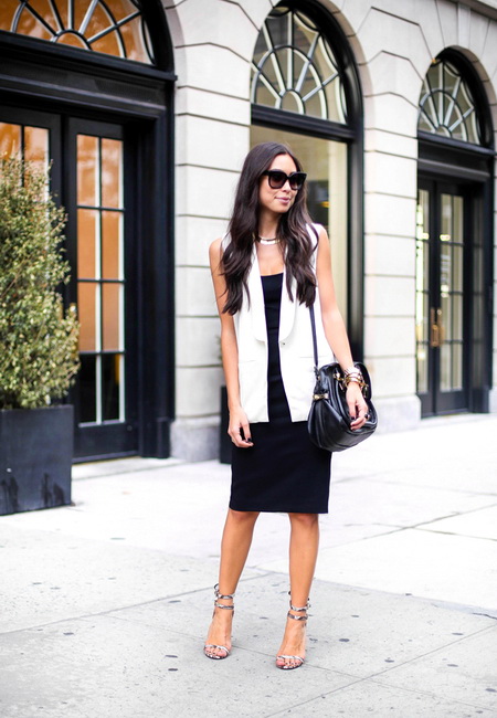 Модный лук: черное платье-комбинация до колен, удлиненный белый жилет, черная кожаная сумочка на длинном ремешке, серебристые босоножки, темные очки и металлические браслеты