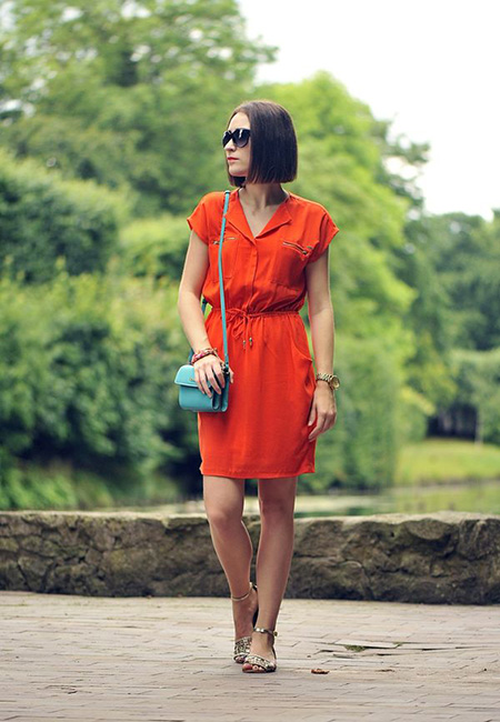 Модный лук: Оранжевое платье-рубашка с кулиской и карманами на молнии, золотистые босоножки с пайетками, голубая сумка-мессенджер, деревянный двухцветный браслет, темные очки