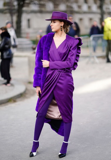 Модный лук: фиолетовое платье с запахом длины миди, плотные фиолетовые колготки, черно-белые босоножки на шпильке с ремешком на щиколотке, фиолетовая шуба из искусственного меха, фиолетовая шляпа с полями и длинные серьги