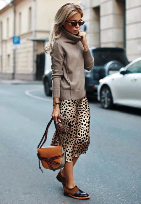 Модный лук: леопардовое платье-комбинация ниже колен, тонкий бежевый свитер с высоким воротом, кожаные черно-коричневые лоферы, маленькая кожаная сумочка на длинном ремешке и треугольные солнцезащитные очки